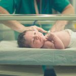 Mass Surrogacy Plot Hits Legal Wall Newborn baby in hospital bassinet being cared for by nurse