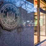 Cartel Gun Pipeline Exposed — 140 Weapons FBI emblem on a stone wall beside a glass entrance