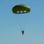 Parachutist descending under a green round canopy