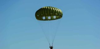Parachutist descending under a green round canopy
