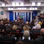 Press Passes Flagged – Chaos At Gates Press secretary at podium addressing reporters in briefing room