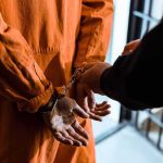 Bomb-Then-Gun Plot Shocks Arizona Prisoner in orange jumpsuit handcuffed by officer