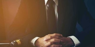 Top War Planner Ousted – Iran Clock Ticks person in suit with hands clasped at a desk beside a gavel