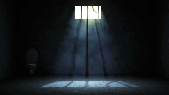 Empty prison cell with light beams through a small barred window