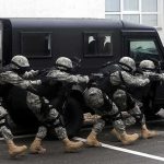 Ex-Spy Boss BUSTED – Treason Shock Tactical team advances beside an armored vehicle