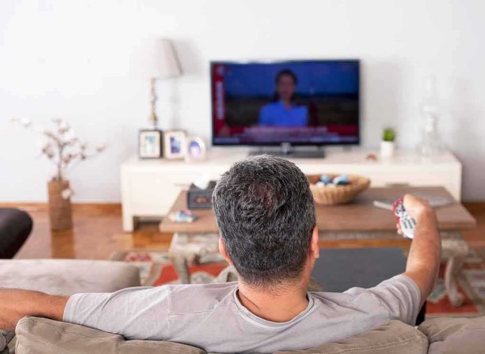 Man watching TV from couch with remote in hand