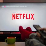 Shocking Cuts At Netflix – Growth Claim Stands TV screen displaying Netflix with person holding remote