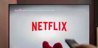 Shocking Cuts At Netflix – Growth Claim Stands TV screen displaying Netflix with person holding remote