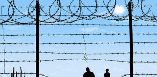 Silhouettes of two people walking by a barbed wire fence