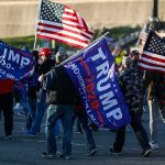 Crowd of people carrying political and American flags at a street gathering