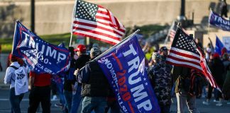 Crowd of people carrying political and American flags at a street gathering