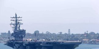 265 Days At Sea – At What Cost? Aircraft carrier escorted by a tugboat in a harbor