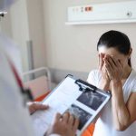 Psych Ward Exit – Death Hours Later Woman covering her face while doctor holds a clipboard in a hospital room