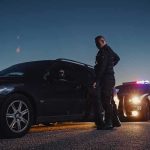 Troop Arrest Sparks DC Gun Uproar Police officer stands beside a stopped car at dusk