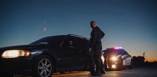 Troop Arrest Sparks DC Gun Uproar Police officer stands beside a stopped car at dusk